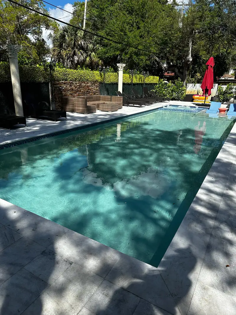 Backyard pool with wicker seating, a red umbrella and mature trees behind