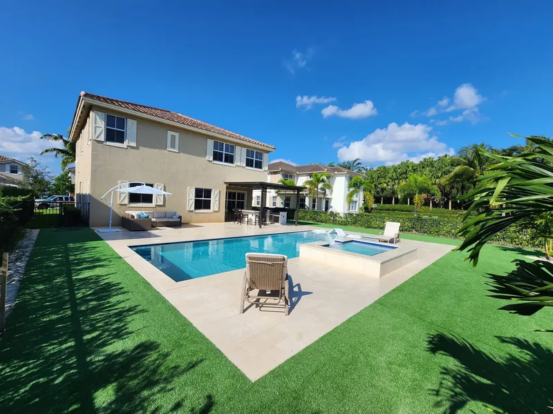 Backyard pool with raised spa, light coping and green turf beside a two-story house