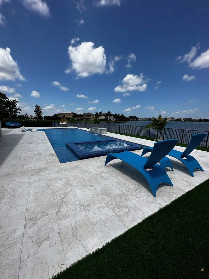 Blue loungers beside a pool with a spa, light stone deck and lake view