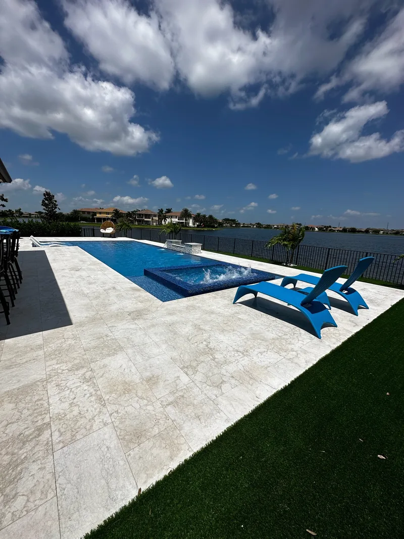 Blue pool with a raised spa, blue loungers and turf along the deck edge