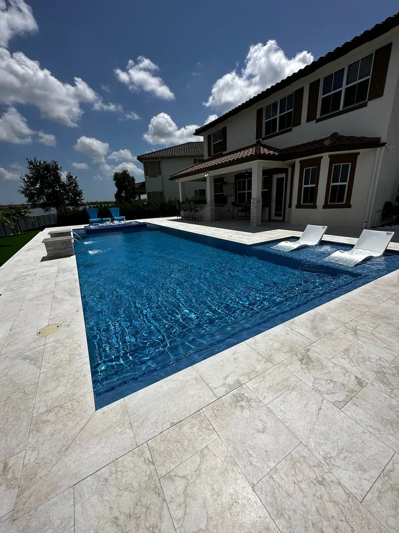 Blue pool with in-pool loungers and a two-story house with a tile roof