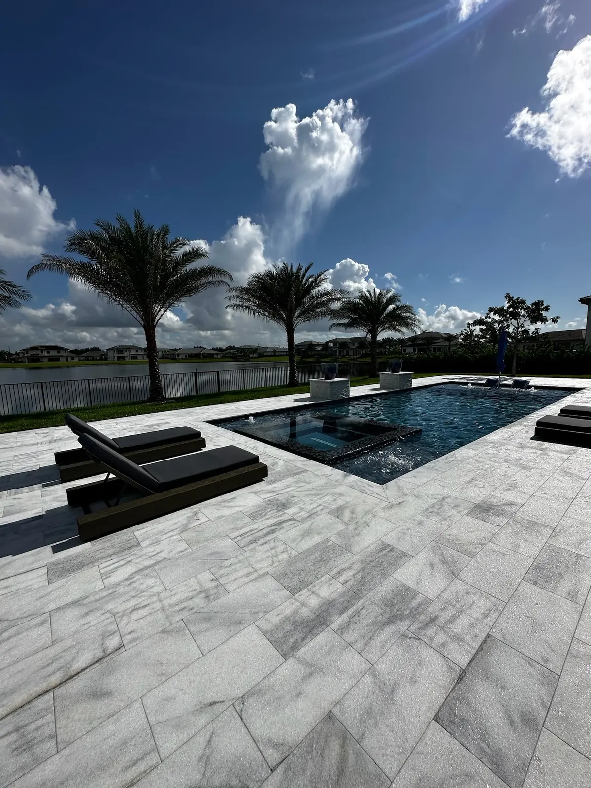 Two dark chaise loungers on a veined stone deck with a pool and lake behind