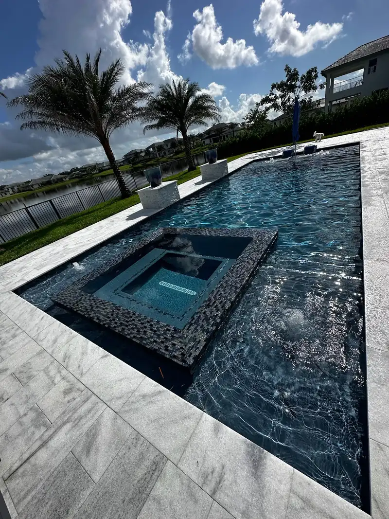 Raised spa island with dark mosaic trim in the middle of a pool beside a lake