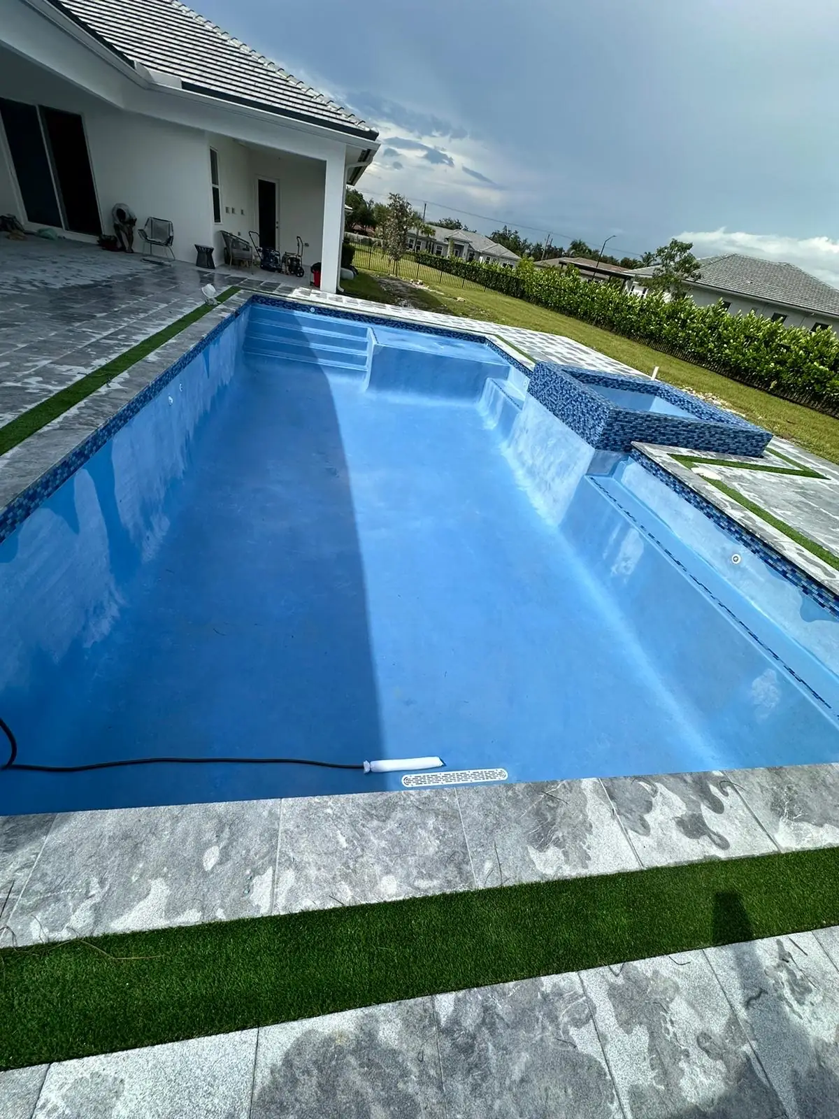Empty pool with new light blue interior finish, steps and a raised mosaic spa on gray pavers