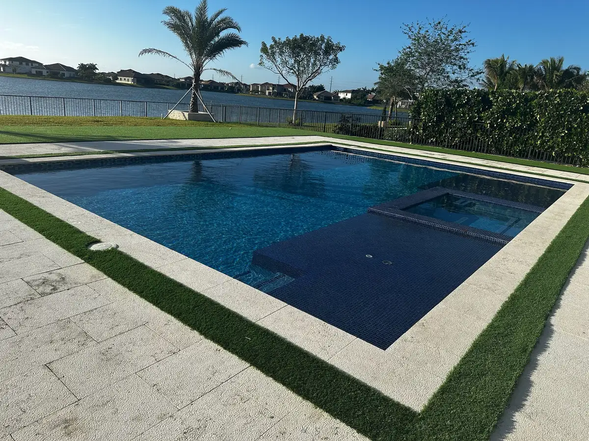 Pool with a raised spa corner and turf edge overlooking a lake with young palms