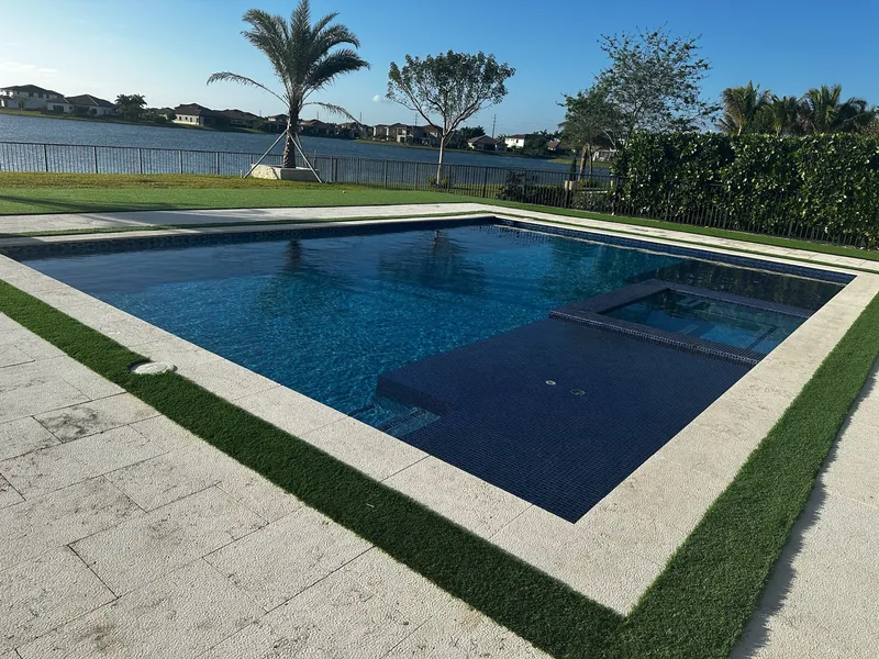 Pool with a raised spa corner and turf edge overlooking a lake with young palms