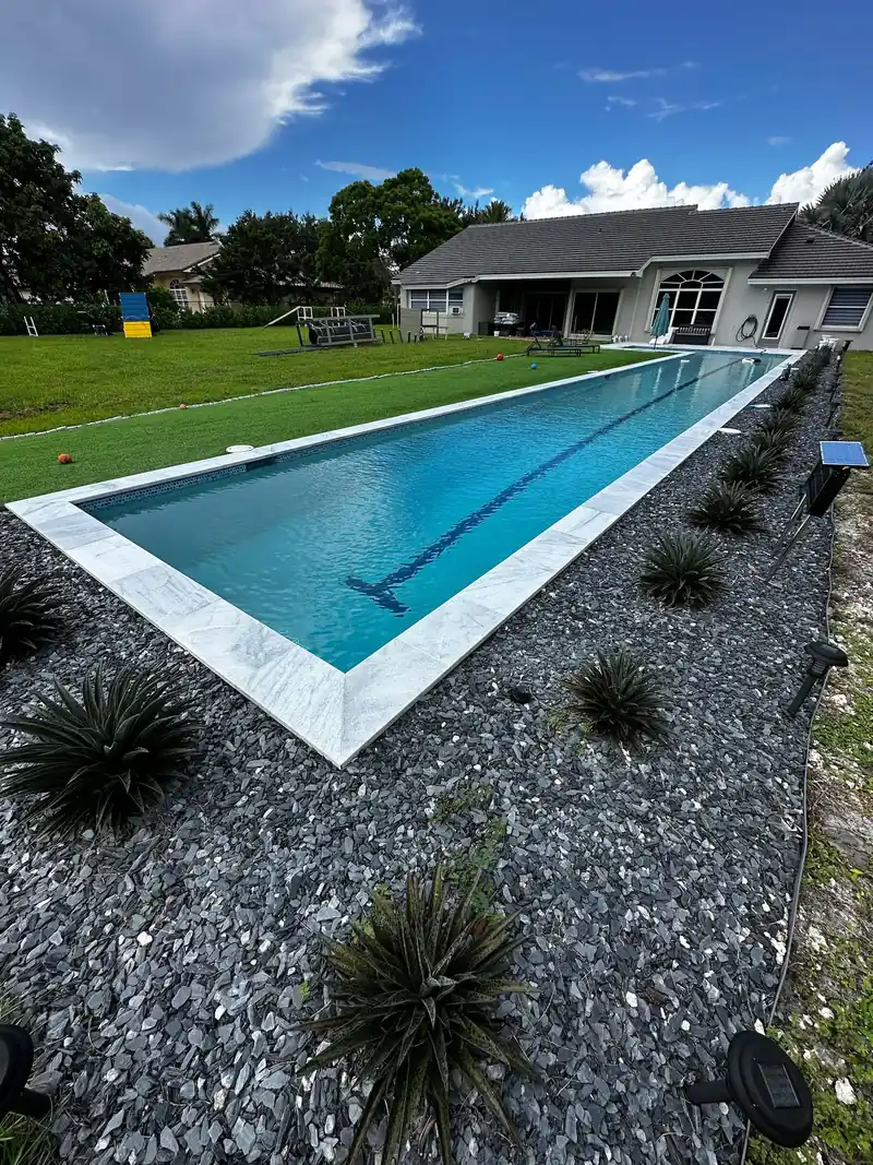 Lap pool with a dark lane line and white coping beside dark gravel and agave plants
