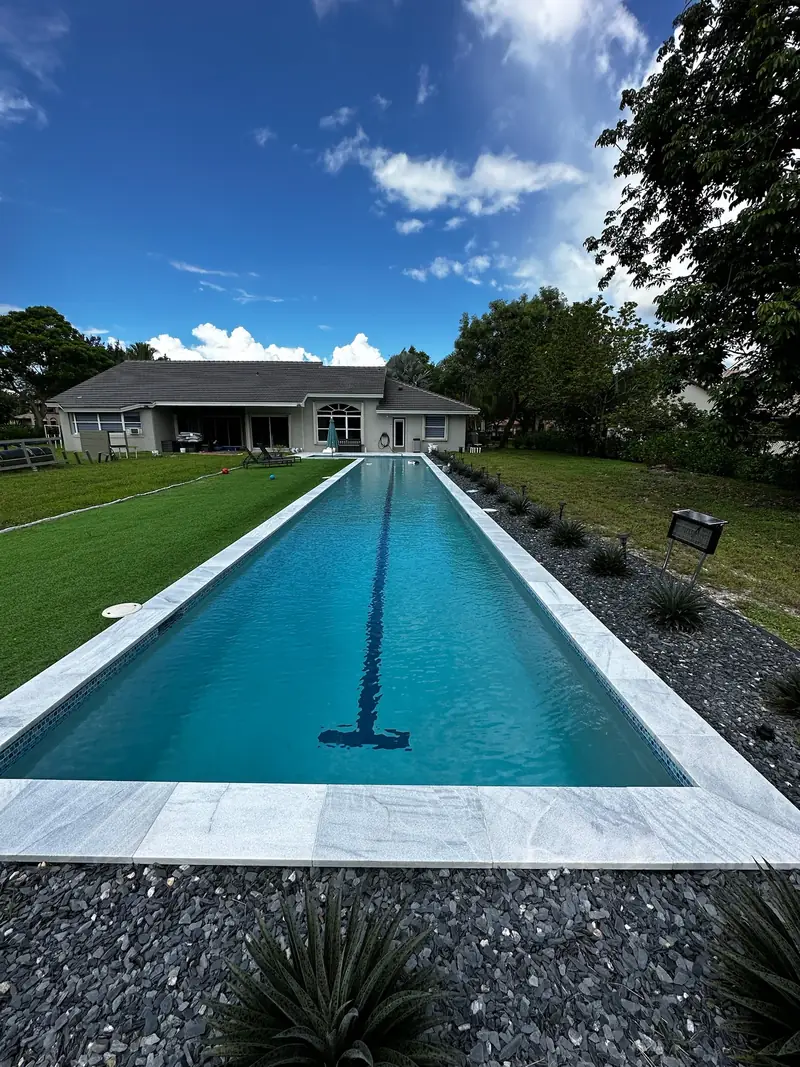 Long lap pool with a lane line and white marble-style coping surrounded by dark slate gravel