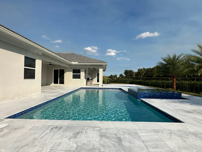 Low-angle view of a pool with mosaic waterline tile and spa beside a white house
