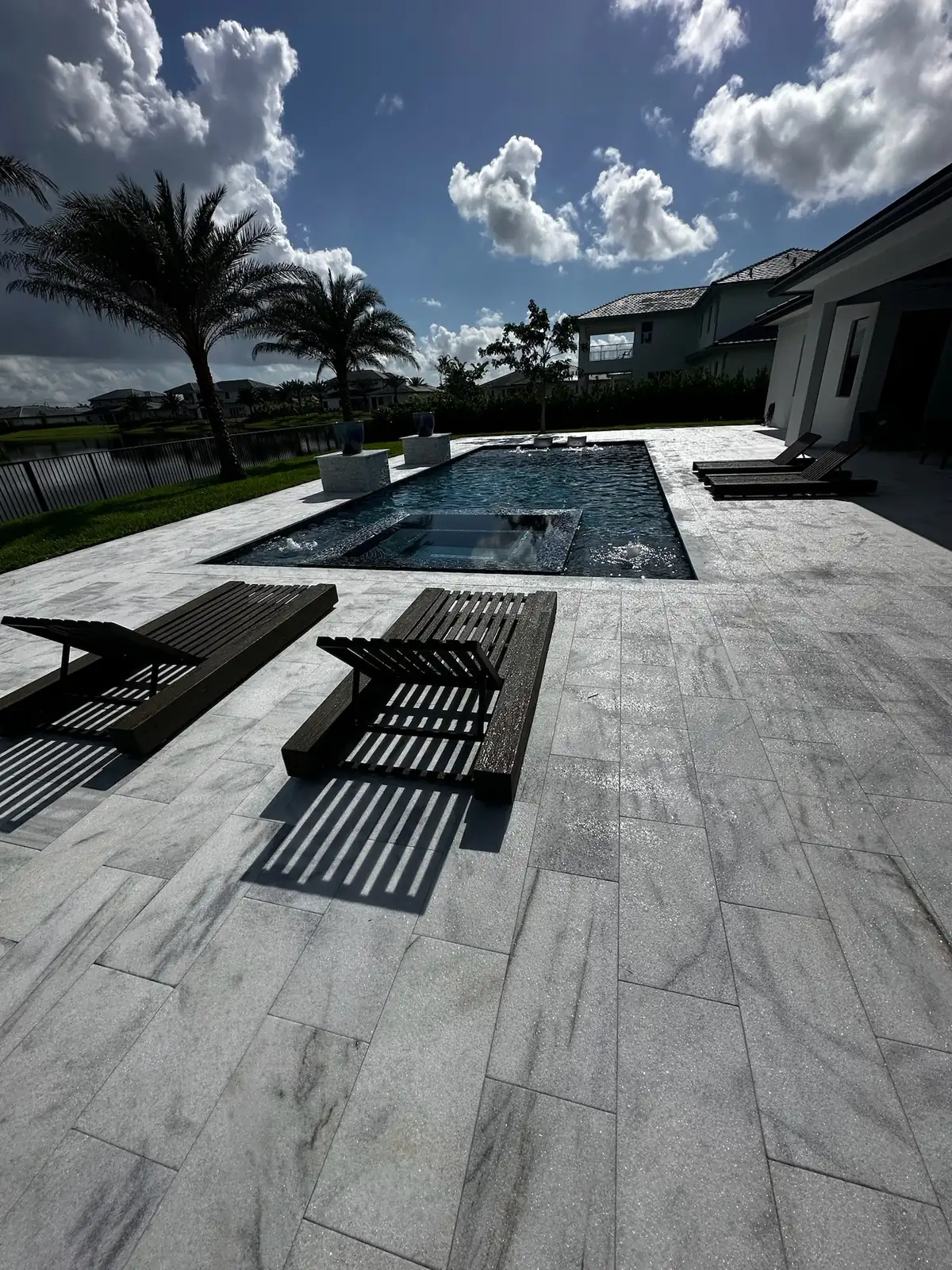 Light veined stone deck with black loungers and a pool with a spa overlooking a lake