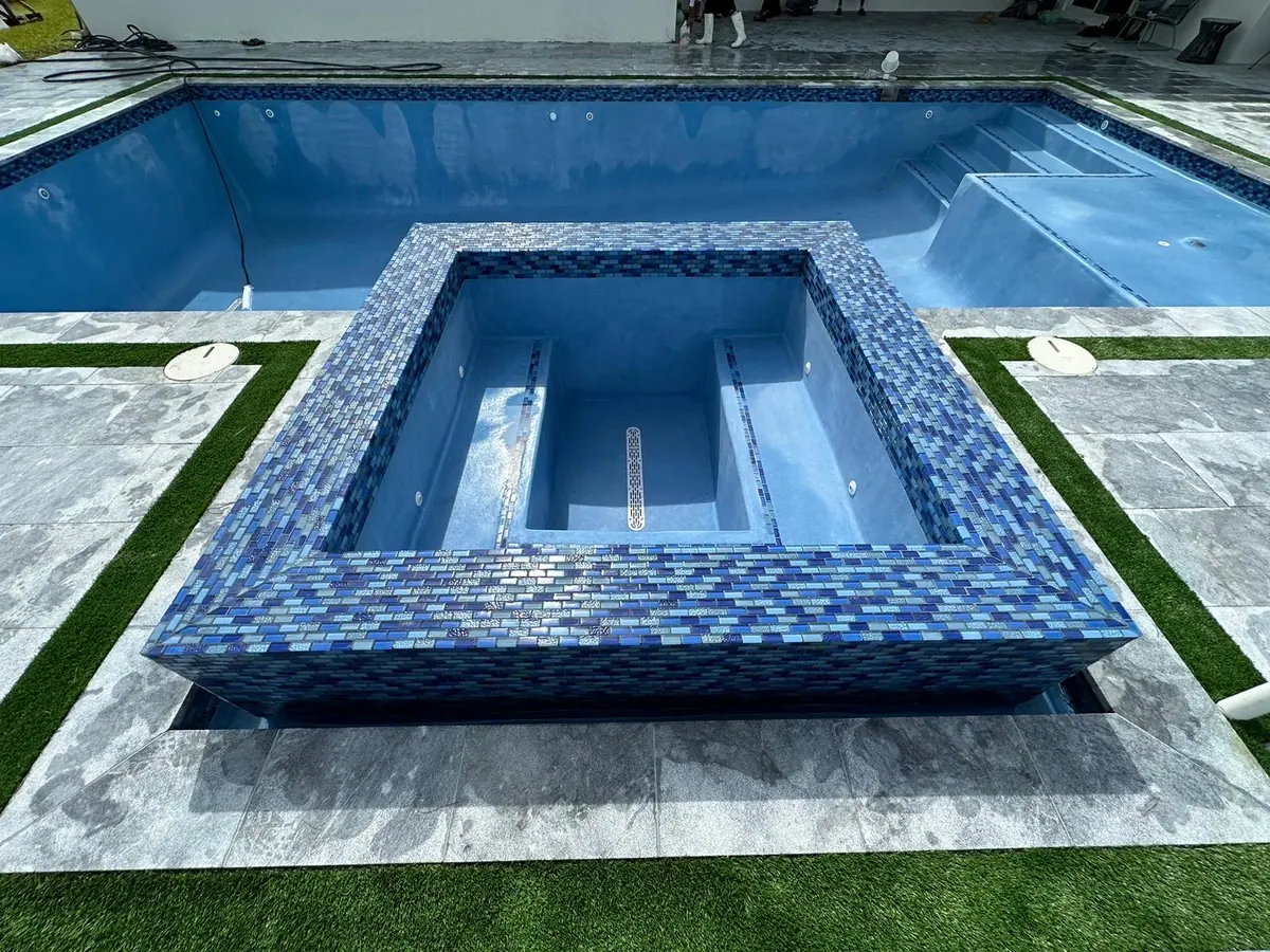 Raised spa with blue mosaic tile and an empty pool, gray stone coping and artificial turf strips