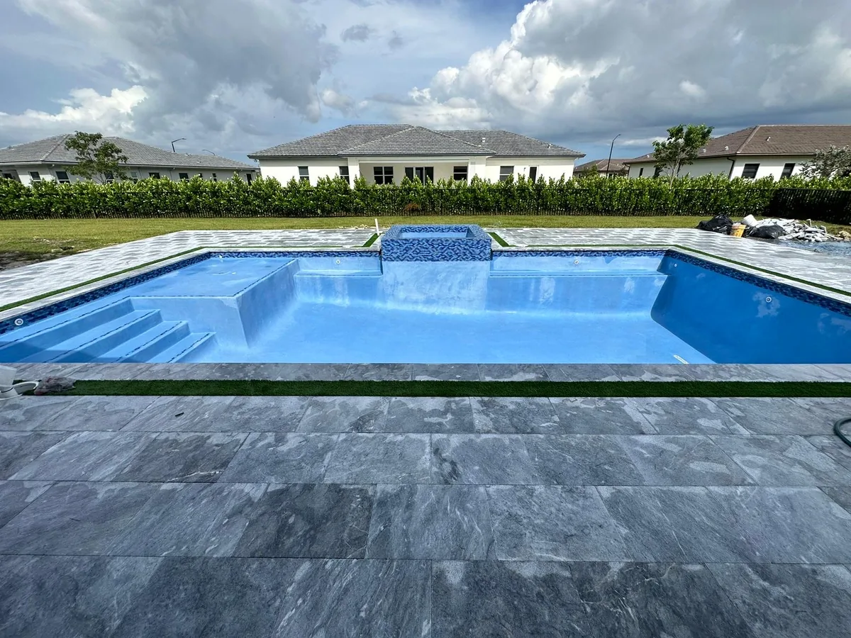 Empty pool with fresh blue interior, entry steps and a raised spa behind dark gray stone pavers