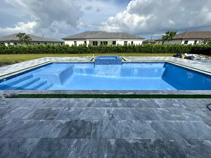 Empty pool with fresh blue interior, entry steps and a raised spa behind dark gray stone pavers