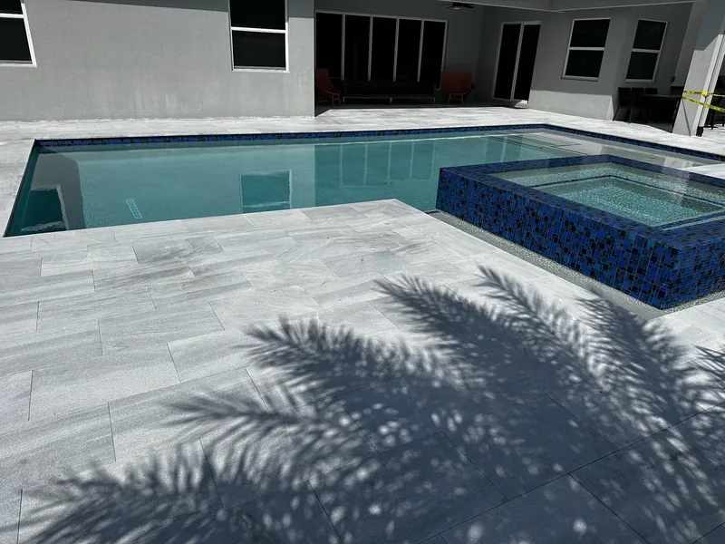 Pool with a blue mosaic spa and light porcelain-style pavers under a palm shadow