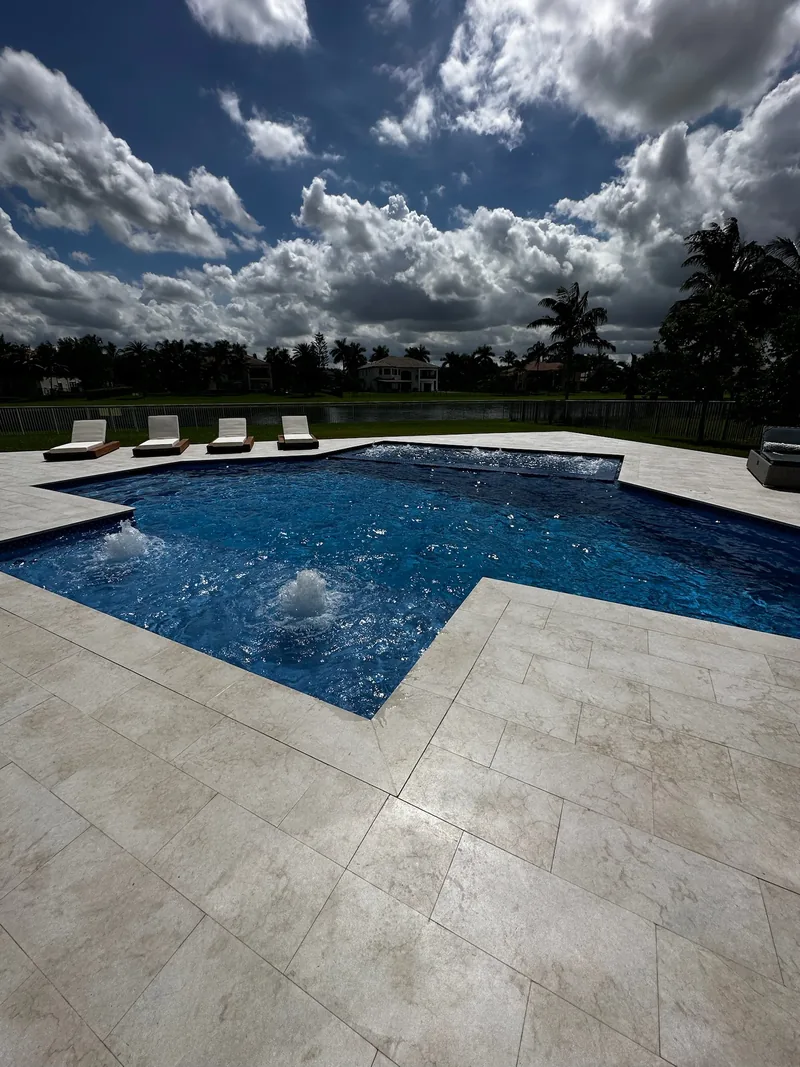 Pool with bubbling deck jets, stepped corner and a row of loungers on beige pavers