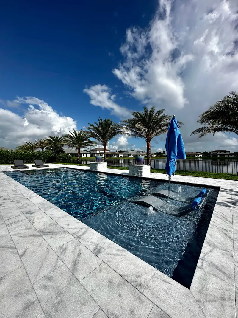Pool with an in-pool lounger under a blue umbrella and veined stone deck