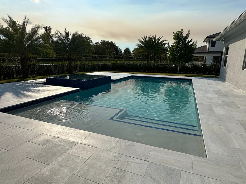Pool tanning ledge with a ripple water feature, mosaic spa and gray pavers at dusk