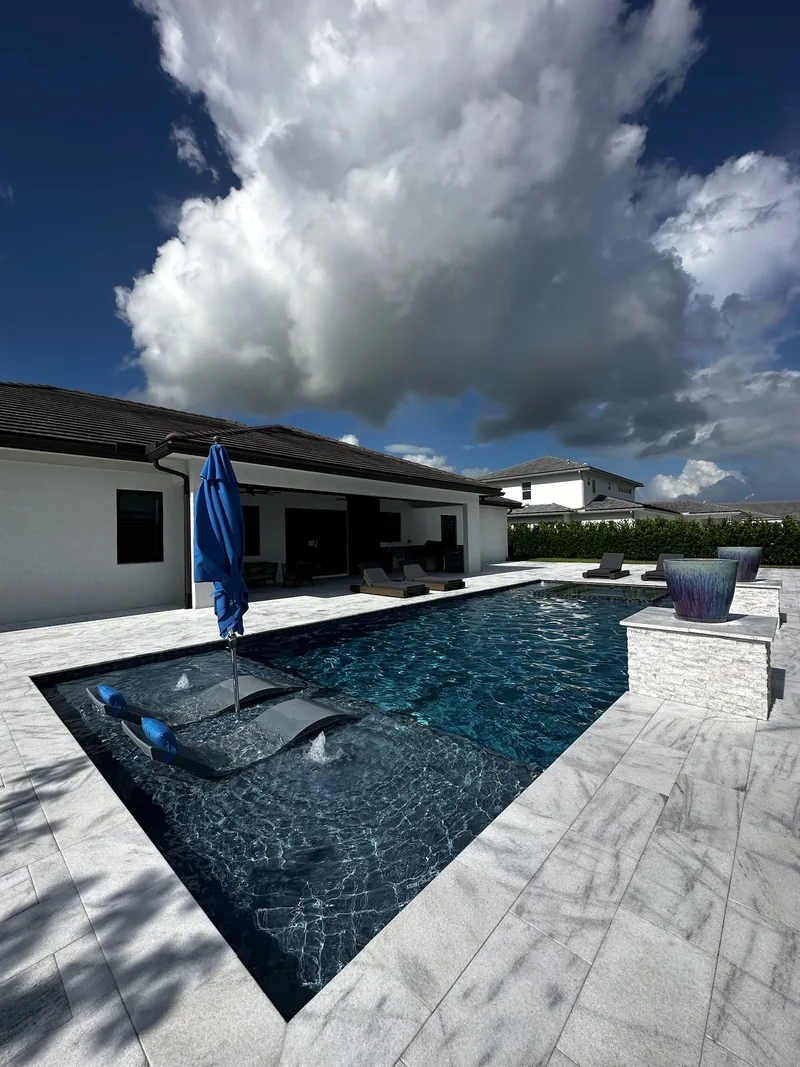 Pool with an in-pool lounger, umbrella and stone-clad water feature at the far corner