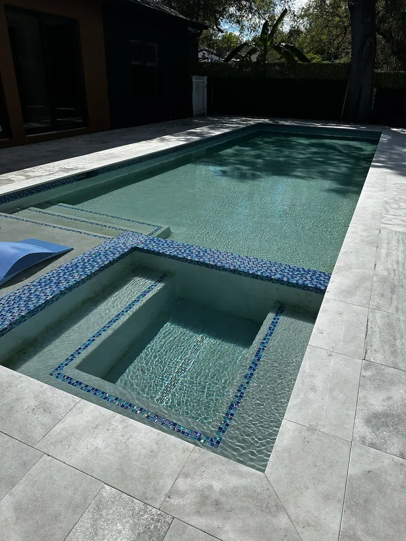 Pool with an inset spa trimmed in blue mosaic tile and gray stone pavers in shade