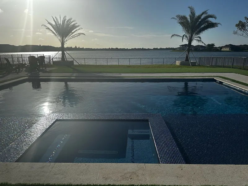 Pool and spa with a mosaic border facing a lake with strong low sun glare