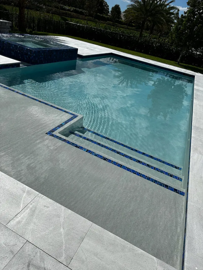 Shallow ledge with blue tile step lines inside a pool bordered by light gray pavers