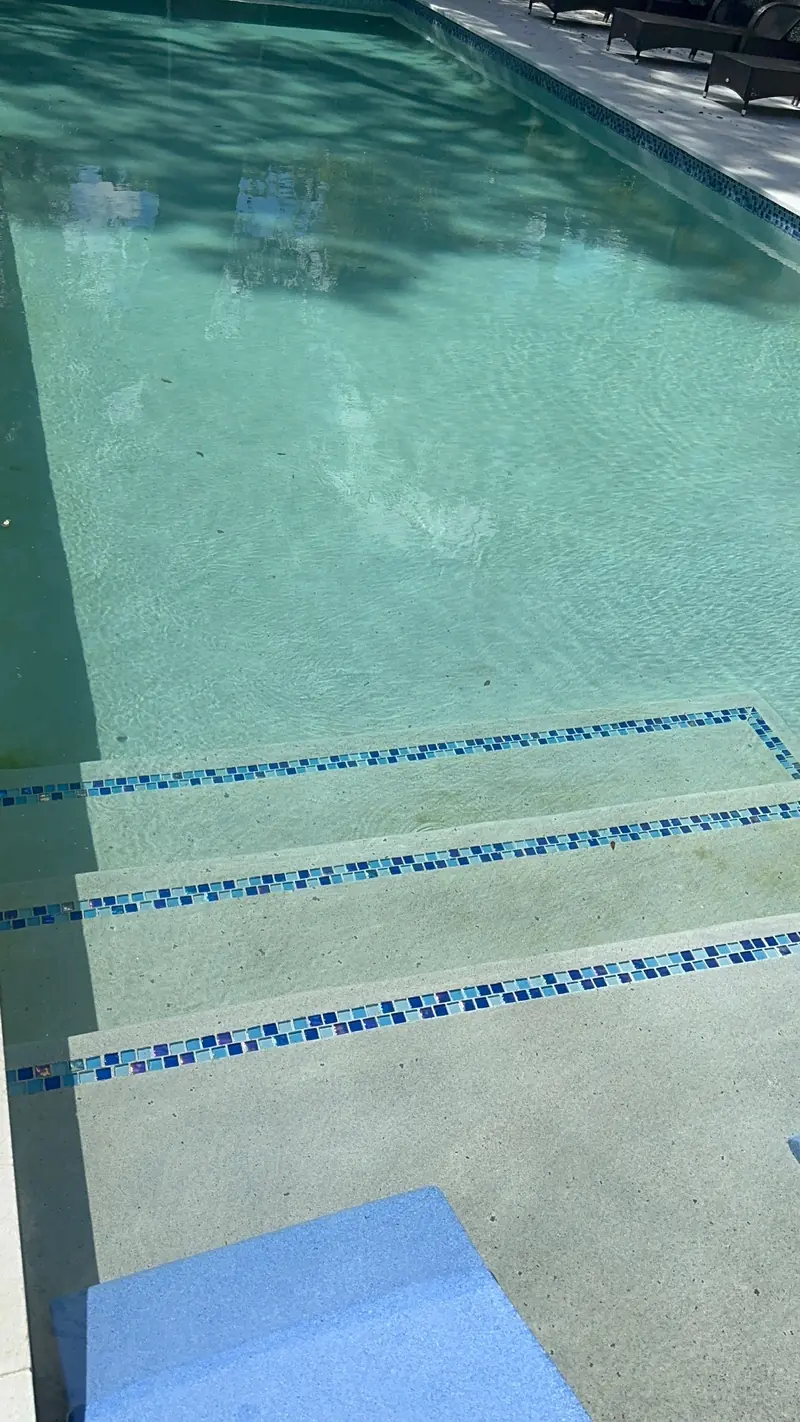 Pool entry steps with blue glass mosaic tile lines on each step and blue foam loungers