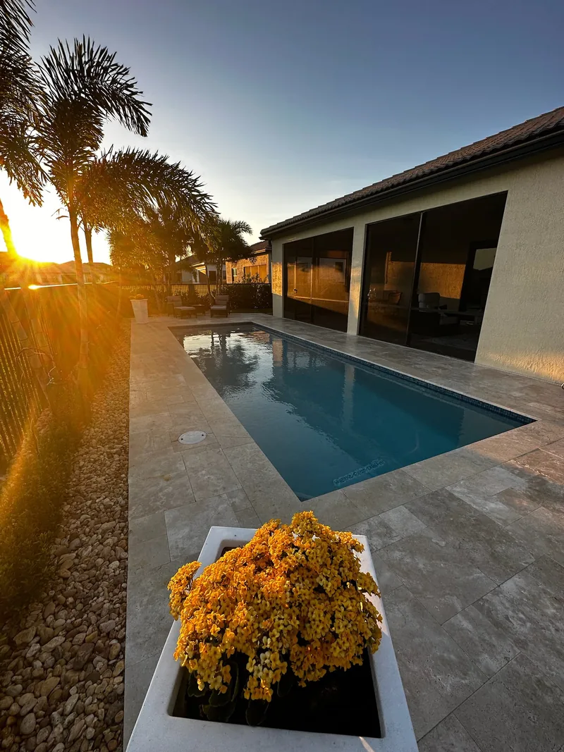 Narrow pool with a flower planter in the foreground and sunset behind a screened lanai