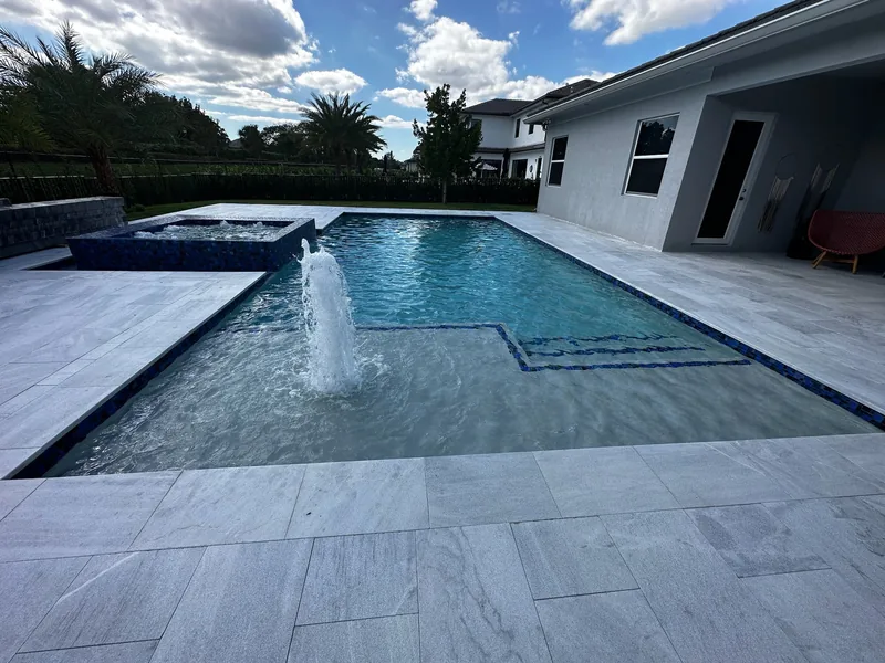 Wide view of a pool with a water jet over the ledge and a raised spa behind