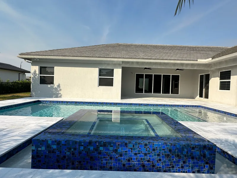 Raised spa wrapped in deep blue mosaic tile in front of a covered patio