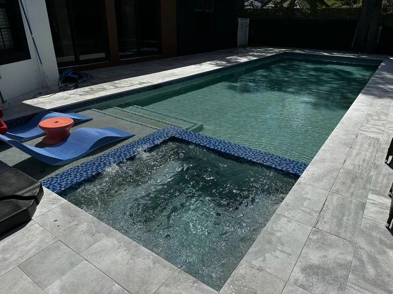 Bubbling spa next to a pool ledge with blue loungers and an orange side table