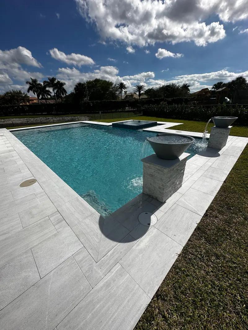 Stone pillar water bowls spilling into a pool with plank-style pavers and a lawn