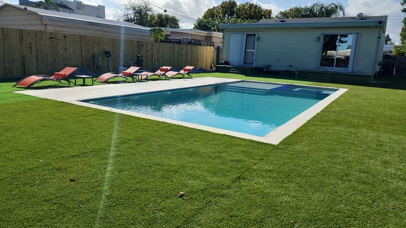 Rectangular pool on a turf lawn with red loungers and a small cottage
