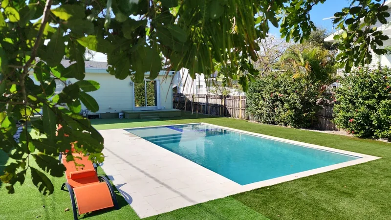 Rectangular pool with light coping on an artificial turf lawn with orange loungers under a leafy branch