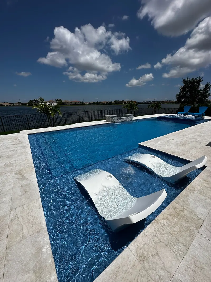 Two white in-pool chaise loungers on a ledge in a rippling blue pool