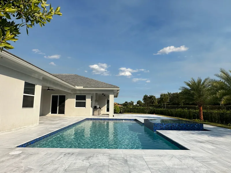 Pool with a blue mosaic spa and light gray pavers beside a white single-story house